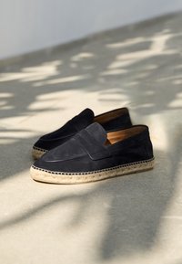 Černé semišové slip-on boty ve stylu mokasín s jutovou podrážkou a prošitými detaily podél okraje.