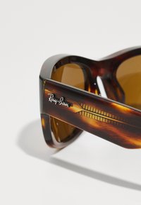Occhiali da sole tartarugati con lenti marroni, caratterizzati da un design elegante e un logo "Ray-Ban" in argento sul lato.