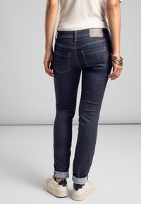 Granatowe dżinsy o dopasowanym kroju, z pięcioma kieszeniami i jasnymi detalami przeszycia. Podwinięte nogawki, zestawione z białymi trampkami.