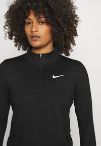 Black long-sleeve pullover made of smooth fabric. Features a high collar and a quarter zip. Notable white Nike logo on the chest.