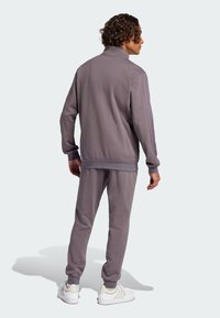 Šedý sportovní teplákový komplet z měkké látky s vysokým límcem, žebrovanými manžetami a slim-fit střihem, doplněný bílými teniskami.