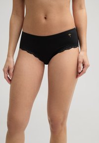 Slip en coton noir avec une bordure en dentelle le long de la ceinture et des ouvertures pour les jambes. Présente un accent brodé à l'avant. Texture lisse.