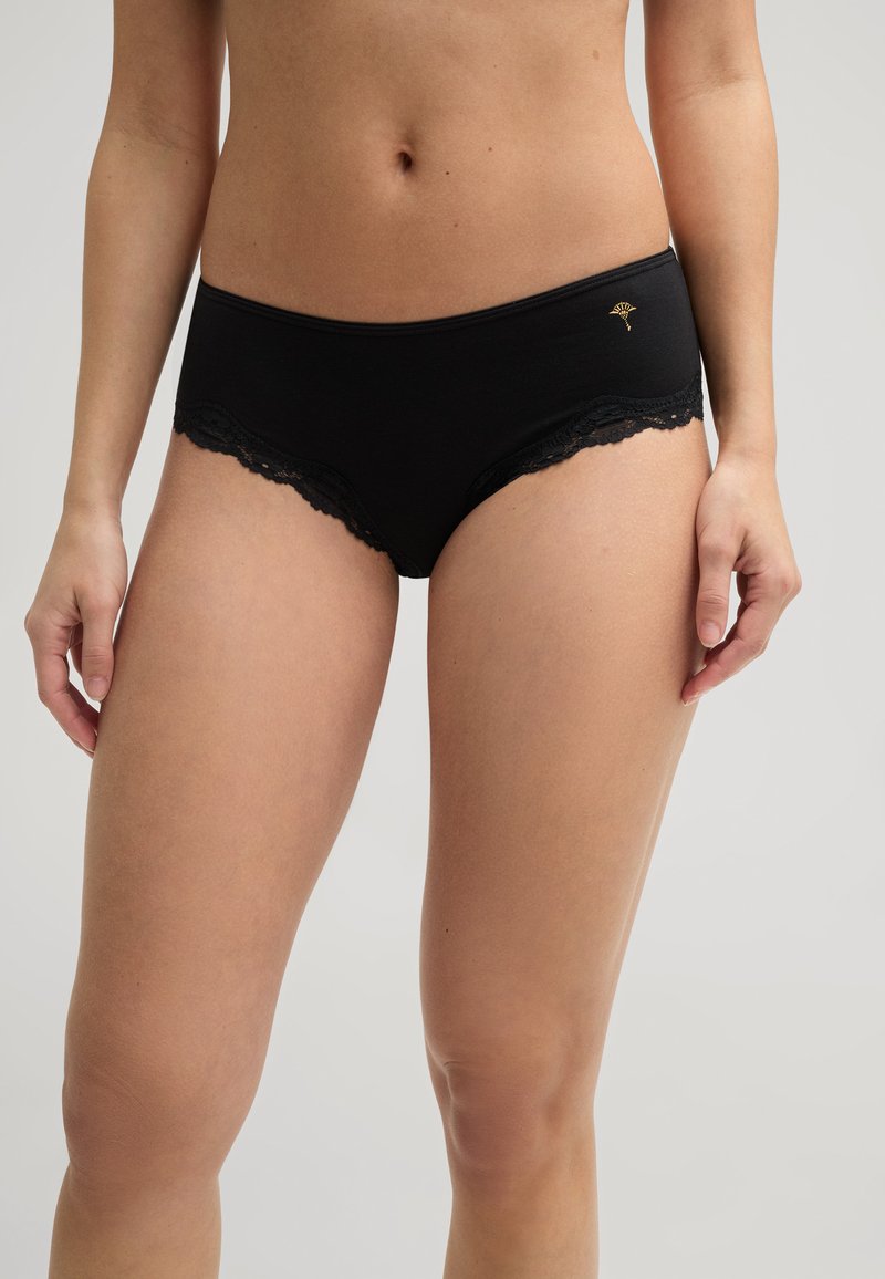 Slip en coton noir avec une bordure en dentelle le long de la ceinture et des ouvertures pour les jambes. Présente un accent brodé à l'avant. Texture lisse.