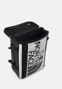 Plecak w czerni i bieli z wodoodpornym wykończeniem. Posiada duże logo, podwójne zamknięcie na zamek oraz regulowane paski boczne. Wnętrze z widocznymi kieszeniami.