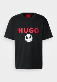 Musta puuvillainen t-paita, jossa on rohkeaa punaista "HUGO"-tekstiä ja valkoinen Jack Skellington -grafiikka. Lyhyet hihat ja pyöreä kaula-aukko.