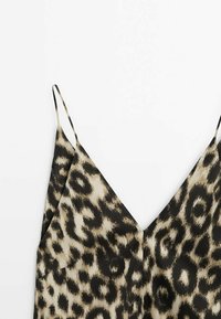 Haut à bretelles spaghetti avec motif léopard beige et noir et un décolleté en V profond sur fond blanc.