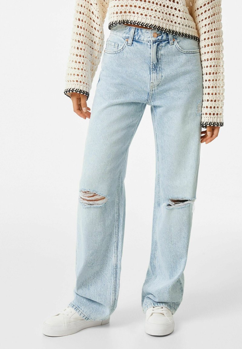 Ljust blå, vida jeans i denim, med slitna knän med fransade kanter, klassisk femfickdesign och knappstängning.