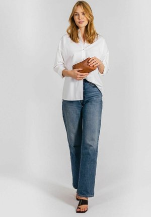 White button-up shirt, relaxed fit, paired with light blue straight-leg jeans, holding a brown leather clutch, worn with black slide sandals.