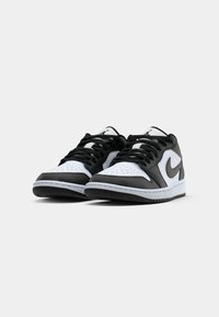 Pár čierno-bielych nízkych Nike tenisiek s šnúrkami, vystavených na hladkom svetlo sivej pozadí, mierne naklonených dopredu.