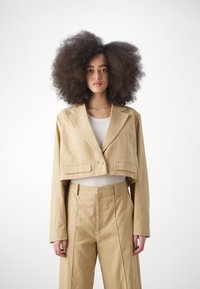 Blazer en lin beige raccourci, avec un seul bouton et des poches à l'avant, assorti de pantalons taille haute et d'un haut côtelé.