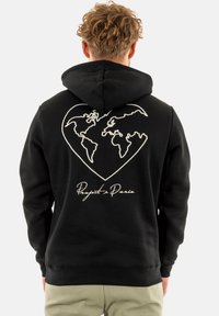 Sweat à capuche noir avec un graphique en forme de cœur représentant le contour d'une carte du monde en blanc. Texte "Project Paris" en cursive en bas. Tissu doux.