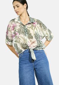Sheer floral shirt with pink and green patterns, button-down front, and tied hem, paired with blue denim high-waisted pants.