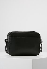 Svart läder crossbody-väska med en texturerad yta, dragkedjestängning och framficka. Utrustad med en avtagbar rem och silverfärgade detaljer.