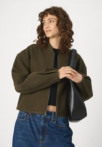 Olive green bomber jacket with a zip front and ribbed cuffs, paired with high-waisted blue denim jeans and a black shoulder bag.