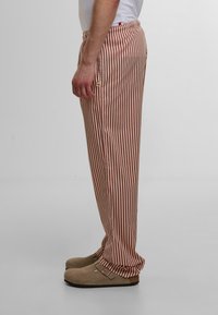 Pantaloni raiati din material roșu și alb, cu talie elastică și buzunare laterale. Textură moale și croi relaxat.