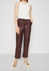 Bordowe skórzane spodnie z elastycznym pasem i sznurkiem, zestawione z dopasowanym białym topem na ramiączkach oraz białymi spiczastymi butami.