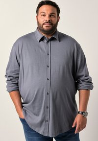 Camicia grigia a maniche lunghe con colletto a punte, realizzata in tessuto testurizzato e con i polsini arrotolati. Abbinata a jeans di denim scuro.