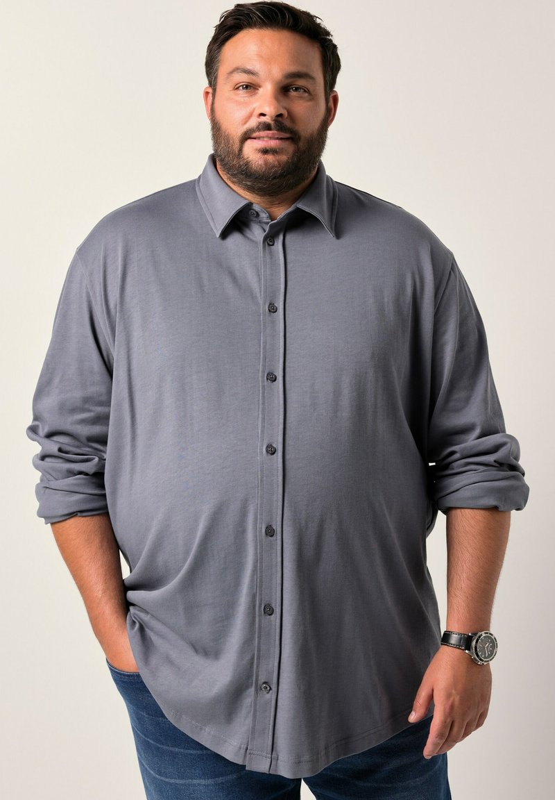 Camicia grigia a maniche lunghe con colletto a punte, realizzata in tessuto testurizzato e con i polsini arrotolati. Abbinata a jeans di denim scuro.