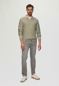 Hellgrüner, strukturierten Pullover mit Kragen, getragen über einem weißen Hemd, kombiniert mit grauen Jeans und weißen Sneakern mit braunen Sohlen.