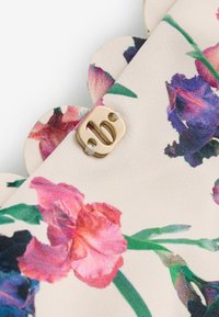 Floral-patterned fabric with scalloped edge and small beige tag featuring a lowercase "b" attached with white thread.