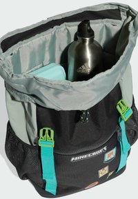 Batoh s tématikou Minecraftu s čiernym základom, sivým vrchom, zelenými prackami, striebornou fľašou na vodu a farebnými záplatami vo vnútri. Bočné strany z textúrovanej sieťoviny.