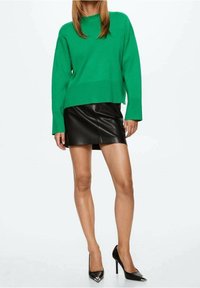 Groene oversized trui met lange mouwen, gecombineerd met een zwart leren miniskirt. Zwarte stilettos met zilveren accenten maken de look compleet.