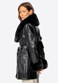 Schwarzer Ledermantel mit einem Kragen und Manschetten aus Kunstfell. Hat eine taillierte Taille, Seitentaschen und eine glatte Textur. Mittellanges Design.