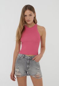 Top corto a coste rosa aderente con collo alto abbinato a pantaloni shorts in denim grigio strappato, con orli sfrangiati e tasche visibili.