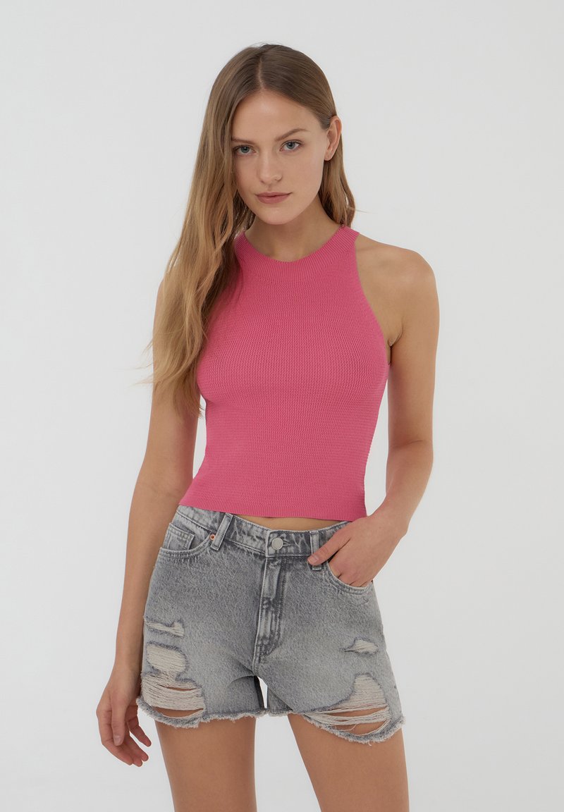 Top corto a coste rosa aderente con collo alto abbinato a pantaloni shorts in denim grigio strappato, con orli sfrangiati e tasche visibili.
