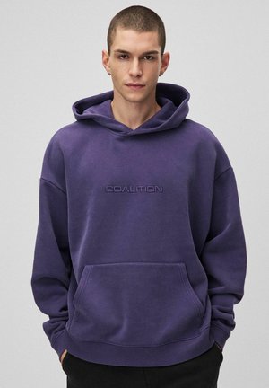 Fioletowa bluza z kapturem, wykonana z miękkiego materiału, z przednią kieszenią, kapturem ze sznurkiem i wytłoczonym logo "COALITION" na klatce piersiowej.