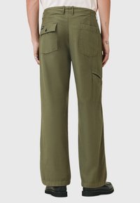 Olijfgroene wijde broek van textuurstof, met twee achterzakken en een zijvak. Zwarte schoeisel maakt de look compleet.