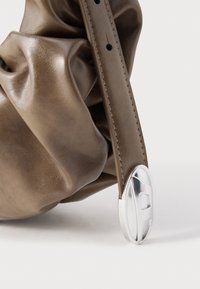 Barna bőr táska összegyűrt textúrával, ezüst ovális csattal, sima felülettel és varrással díszített, rögzített pánttal.