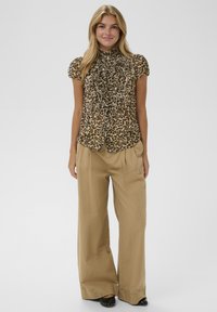 Leopard-print blouse with ruffled front, short sleeves, and a high collar. Worn with beige wide-leg trousers and black shoes.