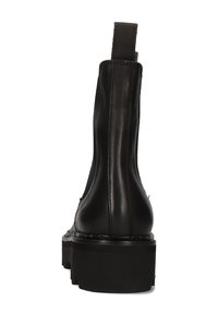 Botín de cuero negro hasta el tobillo con suela gruesa de tipo lug, costuras visibles y una pestaña en la parte trasera, mostrado desde atrás sobre un fondo blanco.