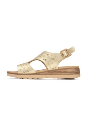 Sandalias de cuña de piel dorada con diseño perforado, punta abierta y correa en el tobillo. Suela marrón clara con detalles texturizados.