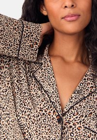 Halka koszula do piżamy w panterkę z czarnym obszyciem, z kołnierzykiem i zapięciem na guziki. Wykonana z miękkiego materiału, prezentująca mieszankę beżu, brązu i czerni.