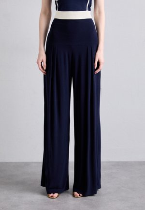 Pantalones anchos de pierna azul marino con una cintura alta de canalé en color crema. Confeccionados con tela suave y plisados verticales, que crean una silueta fluida.