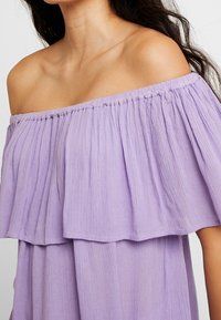 Schulterfreies Kleid aus weichem Lavendelstoff. Verfügt über ein mehrlagiges Rüschendesign mit strukturierter Oberfläche, das das leichte Material betont.