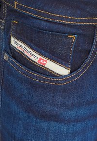 Gros plan sur une poche de jean en denim bleu foncé avec une étiquette blanche indiquant Diesel Industry Denim Division.