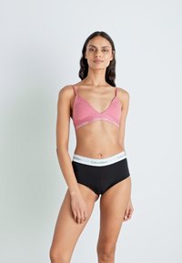 Roza bralette z v-oblikovanim izrezom in nastavljivimi naramnicami, v kombinaciji z visokimi črnimi hlačkami z belim logotipom na pasu.