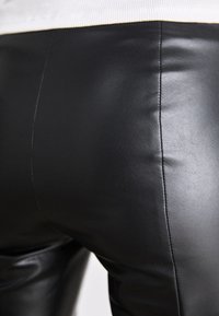 Zwarte leren broek met een gladde, glanzende textuur en een aansluitend ontwerp, met een verticale naad langs de achterkant.
