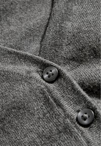 Grauer Strickstoff mit weicher Textur, der schwarze Knöpfe präsentiert. Die Nahaufnahme hebt die Detailgenauigkeit der Knöpfe und das Gewebe des Stoffs hervor.