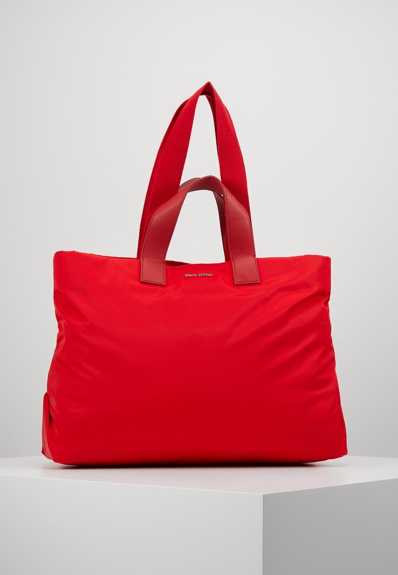 Bolso tote rojo hecho de nailon suave con dos asas de tela resistentes y acentos de cuero. Forma elegante y suave con una mínima marca en la parte delantera.