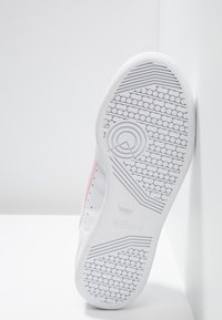 Sneaker bianca con accenti rosa. Inserti in pelle liscia con dettagli perforati. Suola in gomma con un motivo di grip testurizzato e logo del marchio.