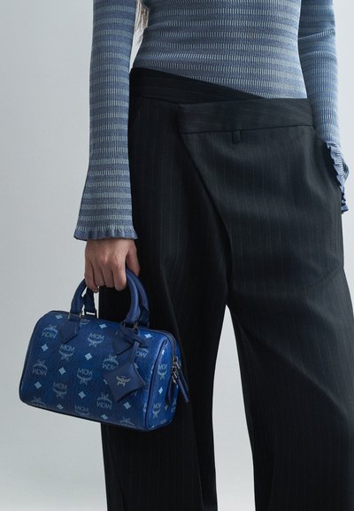 Person wearing blue striped long sleeve top and black pinstripe pants, holding a small blue patterned handbag with dual handles.