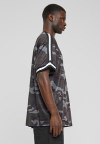 Camiseta de manga corta con patrón de camuflaje en tonos gris oscuro, con rayas blancas en las mangas y un corte suelto y relajado.