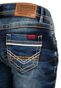 Dunkelblaue Denim-Jeans mit orangefarbener und weißer Stickerei. Verfügt über ein strukturiertes braunes Leder-Patch und ein kleines rotes Markenetikett an der Gesäßtasche.