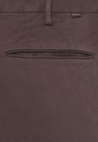 Pantaloni in tessuto marrone scuro con tasca a filetto e una piccola etichetta nera con la scritta "INCOTEX" sopra la tasca.