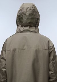 Lichte groene waterdichte jas met een capuchon. Heeft een gestructureerde stof, zichtbare naden en een contrasterend logo op de rug gedrukt.