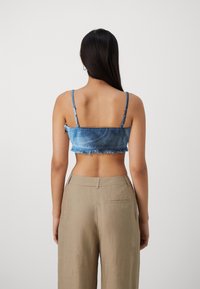 Top recortado de mezclilla azul con dobladillo deshilachado y tirantes ajustables, combinado con pantalones de pierna ancha beige que tienen un bolsillo trasero.